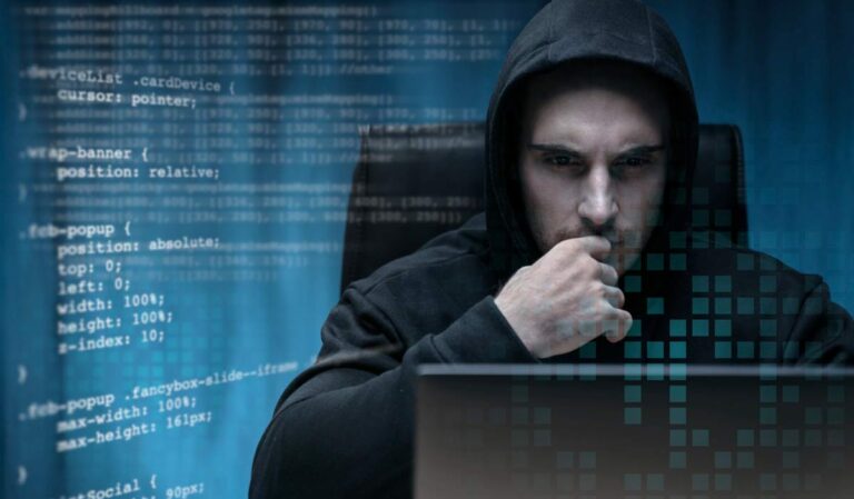 Hacker in a hoodie using a laptop with code in the background, representing cybersecurity threats and the importance of website security tips 2025